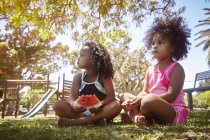 Дві молодші сестри, сидячи на траві, їдять кавун — стокове фото