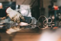 Hands of metalworker cutting copper sheet with electric hand shears at forge workbench — Stock Photo