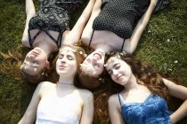 Чотири дівчинки-підлітки в ромашкових головних уборах лежать на парковій траві — стокове фото