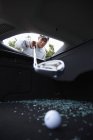 Golfer using golf club to retrieve golf ball through smashed car window — Stock Photo