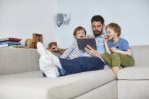 Батько і сини на дивані за допомогою цифрового планшета — стокове фото