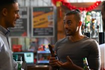Young man in public house holding beer bottle talking to friend — Stock Photo
