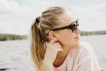 Woman wearing sunglasses looking over her shoulder to lake, Orivesi, Finland — Stock Photo