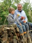 Uomo e ragazzo con le mele, seduto su tronchi — Foto stock