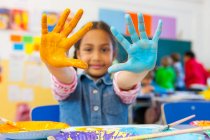 Portrait of primary schoolgirl with painted hands in classroom — Stock Photo
