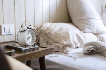 Unmade bed, alarm clock on bedside table — Stock Photo