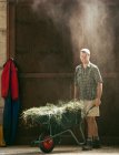 Portrait de jeune ouvrier agricole avec brouette dans une grange agricole poussiéreuse — Photo de stock