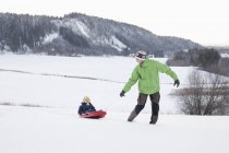 Отец и сын играют на санях в снежном поле — стоковое фото