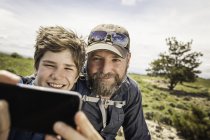 Close up of father and teenage son taking smartphone selfie on hiking trip, Cody, Wyoming, USA — Stock Photo