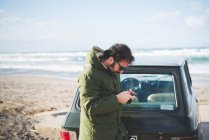 Uomo con auto d'epoca in spiaggia a leggere testi da smartphone, Sorso, Sassari, Sardegna, Italia — Foto stock