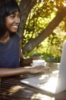 Молода жінка сидить на відкритому повітрі, використовує ноутбук, п'є каву — стокове фото