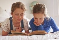 Two sisters lying on bed reading a book — Stock Photo