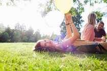 Portrait of young woman lying on grass with balloon at park party — Stock Photo