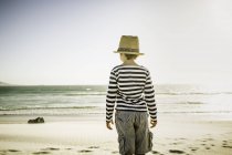 Мальчик стоит на пляже, смотрит на море, вид сзади — стоковое фото
