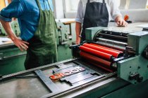 Senior Handwerker / Techniker, der den jungen Mann auf der Buchdruckmaschine in der Buchkunst-Werkstatt betreut, mittlere Sektion — Stockfoto