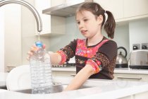 Ragazza che riempie la bottiglia d'acqua in cucina — Foto stock