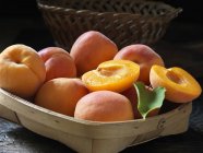 Whole and halved king apricots with leaf in basket — Stock Photo