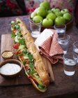 Tandoori chicken baguette and glasses of water on wooden table — Stock Photo