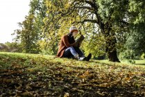 Молодая женщина сидит на траве в парке, учится, вид с низкого угла — стоковое фото