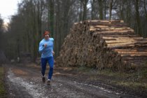 Full length view of runner running on treelined path by stack of logs — Stock Photo