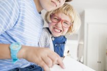 Girl pulling face whilst reading with brother in kitchen — Stock Photo