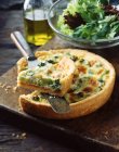Broccoli quiche and salad leaves on wooden chopping board — Stock Photo