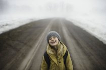Portrait of girl in knit hat standing in middle of foggy dirt road laughing — Stock Photo