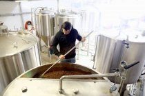 Lavoratore in birreria, mescolando cereali d'orzo nel serbatoio di birra — Foto stock