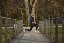 Full length side view of woman on wooden path, hands on hips lunging — Stock Photo
