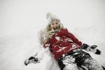 Menina sorridente deitada de costas e coberta de neve — Fotografia de Stock