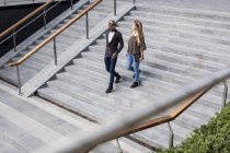 Caucasian woman and African ethnicity man walking down stairs — Stock Photo