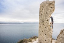 Male rock climber climbing ruined tower on coast, Cagliari, Italy — Stock Photo