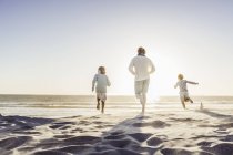 Visão traseira do pai e das crianças que correm na praia — Fotografia de Stock
