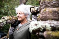 Mature woman carrying log on her shoulder in garden — Stock Photo