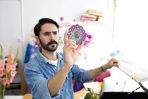 Junge männliche Designerin hält Kreisdruck in Druckereistudio hoch — Stockfoto