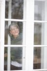 Old woman looking out a window — Stock Photo