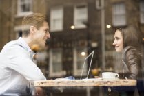 Young businessman and woman with laptop talking in cafe — Stock Photo