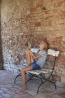 Fille assise sur un banc écoutant de la musique dans des écouteurs, Buonconvento, Toscane, Italie — Photo de stock