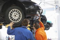 Visão traseira de estudantes de mecânica universitária inspecionando embaixo do carro — Fotografia de Stock