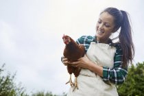 Frau hält Huhn in der Hand vor blauem Himmel — Stockfoto
