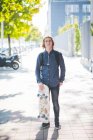 Портрет самоуверенного молодого городского скейтбордиста, стоящего на тротуаре — стоковое фото
