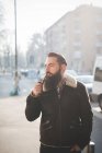 Молодий бородатий чоловік палить трубу на вулиці — стокове фото