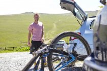 Radler mit Fahrrad im Autoschuh blickt lächelnd in die Kamera — Stockfoto