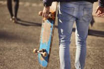 Young man walking outdoors, carrying skateboard, rear view, low section, Bristol, UK — Stock Photo