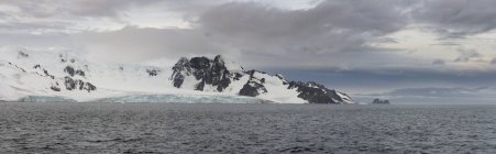 Vista panorâmica de montanhas cobertas de neve e mar sob céu nublado — Fotografia de Stock