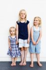 Retrato de três jovens irmãs em pé na frente da parede branca — Fotografia de Stock
