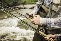 Cropped view of couple holding fishing rods and smartphone by river — Stock Photo