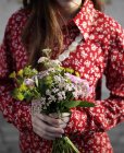 Cropped shot of woman wearing red floral blouse holding bunch of flowers — Stock Photo