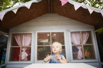 Bébé fille assis à la table en face de la maison de jeu et regardant loin — Photo de stock