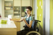 Mulher em cadeira de rodas, trabalhando em restaurante, segurando tigela de comida — Fotografia de Stock